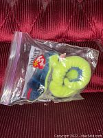 Ty Beanie Baby Hissy the snake plush toy coiled inside a clear plastic Ziploc storage bag against a red fabric background, tags visible within bag.