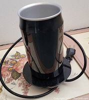 Electric milk frother in black with cord and plug, cylindrical shape.