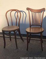 Two bent wood chairs shown side by side against a light background. The left chair has a rounded backrest and circular seat. The right chair has a vertical slatted backrest and perforated seat.