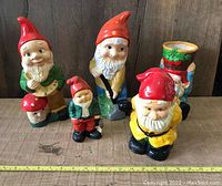 Front view of 5 vintage garden gnome figurines with tape measure indicating size