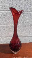 Full view of the tall ruby glass vase with a fluted neck and a bulbous base featuring controlled bubble inclusions inside the glass.