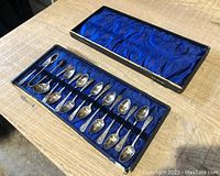 Photo of entire 15-piece set of antique spoons arranged in original blue satin-lined case with lid open and placed adjacent.