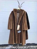 Front view of coffee brown mink fur coat hanging on metal stand.