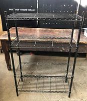 Front view of entire black steel bakers rack showing four wire shelves and tubular legs.