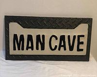 Front view of a metal Man Cave sign displaying embossed diamond plate texture and centered 'MAN CAVE' lettering on a white panel.