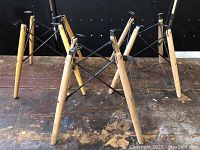 Two Eames style Eiffel Tower bases showing wooden legs and black metal cross supports from an angled view.