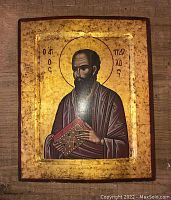 Front view of gilded religious icon showing saint holding book with Greek text.