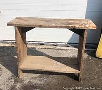 Side view of light brown wooden high farm bench with visible wear and lower shelf
