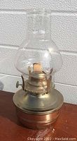Side view of brass hurricane oil lamp on a wooden surface, showing the metal base, burner with wick and the clear glass chimney.