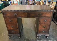 Front view of the brown wooden kneehole desk showing top drawers and carved clawed feet