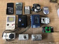 Full lot overview showing 13 electronic items including gaming device, cameras, calculators, cassette player and headlamp flashlight.