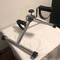 Side angle of pedal exerciser showing welded metal frame, foot pedal, and adjustment knob