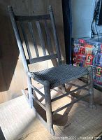 Front angle view of the wooden rocking chair showing vertical backrest slats and woven seat.
