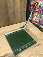 Angle view of the full paper cutter showing the green base, metal arm, and handle.