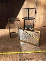 Five display pieces including a tall glass cube, three smaller glass cubes, and one mirror tray on wooden surface with measuring tape for scale.