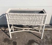 Front view of white wicker planter elevated on a wicker stand, showing the woven design and steel liner inside.