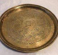 Top-down image of the entire brass tray showing circular shape, hammered texture, and detailed stamped decorations along the edge and center.