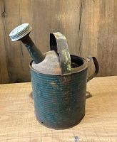 Front side view of vintage tin watering can showing ribbed cylindrical body, curved handle, and perforated spout.