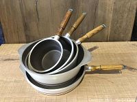 Side view of stacked pots and pans showing wooden handles and inside surfaces.