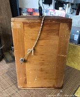 Outer view of the wooden lock box showing wood grain, metal lock, and attached rope with key.