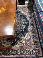 Area rug with navy blue background, floral medallion design, placed under a wooden coffee table and between plaid upholstered furniture.