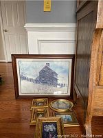 Large framed winter scene barn print with five smaller gold framed artworks on floor