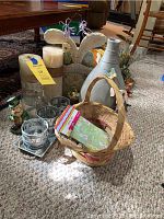 Various decorative items arranged on carpet including two large pillar candles wrapped in burlap, small votive candle holders with stones in a tray, gray vase with butterflies, Easter bunny decor, and wicker basket with colorful napkins.