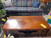 Top angled view of wooden coffee table in front of a plaid couch, showing decorative inlay and overall condition.