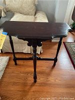 Front three-quarter view of dark walnut foyer table showing scalloped edges, turned legs, and apron detail.