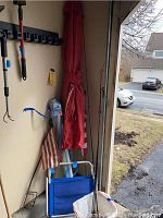 Photo shows three fishing rods, large red umbrella, blue beach chair, and American flag packed in a garage or storage space.
