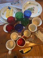 Full set with Holiday Hostess Christmas china plates, colored glass goblets in red, green, and blue, white coffee mugs including one with red and peppermint details, and clear glass pitcher with Christmas tree design