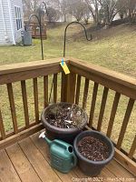 View of two brown planters filled with soil, green watering can placed in front on deck.