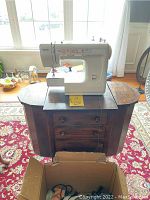 Full view of the sewing machine placed on the antique sewing table with three drawers and a fold-out top surface.