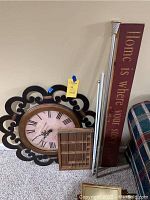 Decorative wall clock, hanging thimble display, wall sign and two curtain rods arranged on carpeted floor near couch and wall outlet.