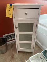 Front view of white cabinet showing drawer and glass-paneled cabinet door with round knobs.