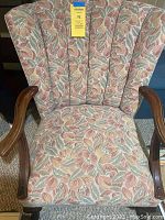 Front view of floral fabric wing chair with wooden armrests showing fabric pattern and backrest design.