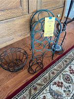 Four black wrought iron items grouped together: a round bowl, wine rack, napkin holder, large candle holder, all with circular and spiral design motifs, displayed on wooden floor.