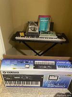 Yamaha EZ-220 keyboard set on stand with keyboard box beneath, and several books on the keyboard.