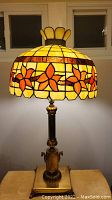 Full view of Tiffany style 3-way lamp lit, showing stained glass shade with yellow and orange flower design, brass base and stand.