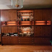 Full frontal view of the wall unit lit from within showing multiple cabinets, drawers, and glass display sections filled with glassware and china.