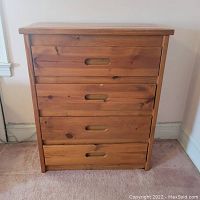 Front view of wooden dresser with four drawers closed, showing wood grain and natural finish.