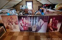 Four large glass poster frames leaning against a wall in a cluttered attic space, featuring floral and cosmetics posters.