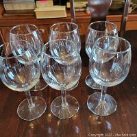 Photo showing six clear glass wine glasses arranged on a wooden surface, all in excellent condition.