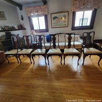 Front view of six wood dining room chairs aligned in a living room with a couch and decorative curtains in the background.