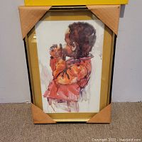 Framed watercolor painting of a child with dark hair, side profile, holding an object near mouth. Frame is gold-colored and protected by cardboard corners.