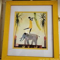 Framed unsigned tropical artwork featuring a child playing a flute while standing on an elephant, with palm trees in the background.