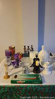 Photo showing assorted candle holders, candles, glass vases, and tranquility fountain items including brass candelabra, purple textured candle holders, and clear glass containers.