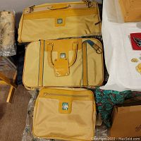 Three yellow-beige Avon luggage bags arranged on the floor, visible logos, and tan handles.