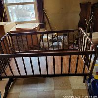 Wood baby bassinet viewed from a side angle showing the rocker design and spindle turned rails.