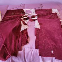 Seven burgundy velor valances arranged on a pink surface, showing rich texture and included metal hangers.